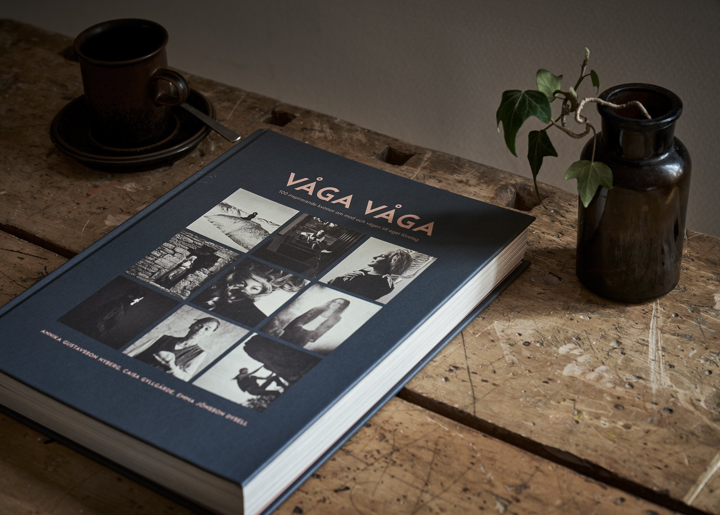 Boken 'Våga Våga' på ett träbord med kaffekopp och vas