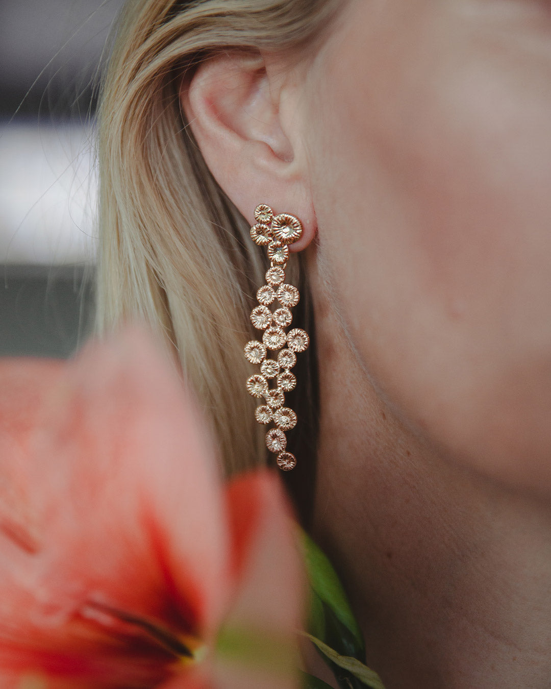 Knappkorall örhänge på örat, med blomma i förgrunden